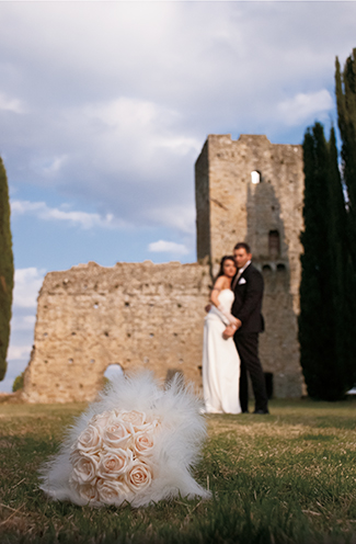 # The bride and the groom together in the castle graveyard. Focus on the bouquet on the grass (Castello di Romena, Casentino, Tuscany).